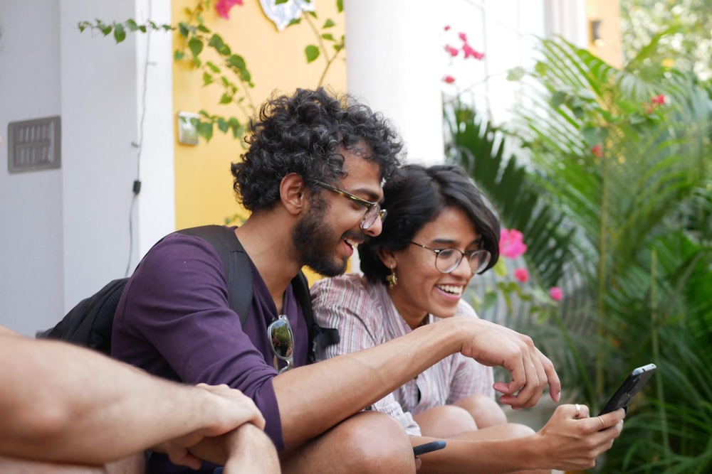 Dua orang tertawa sambil melihat layar ponsel bersama, melambangkan program referral
